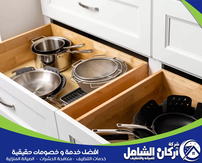 درجان مطبخ مفتوحان يحتويان على أواني طهي ومقالي ومصافٍ مرتبة داخل خزائن خشبية بشكل منظم.