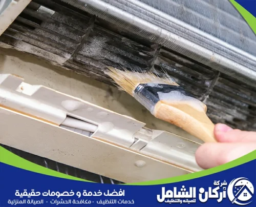 توضح تنظيف المبادل الحراري الداخلي للمكيف باستخدام فرشاة، مع إزالة الأتربة المتراكمة بين الزعانف لتحسين كفاءة التبريد وتدفق الهواء.