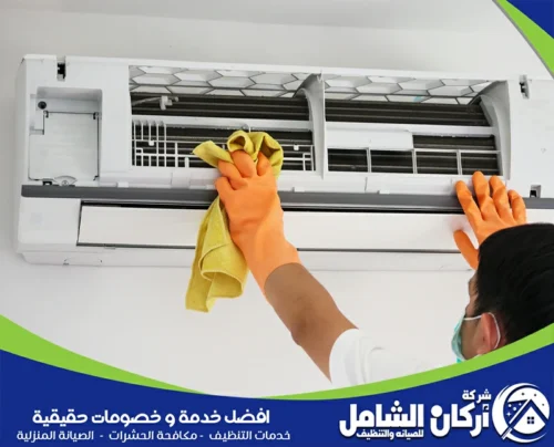 عاملًا يرتدي قفازات وينظف الوحدة الداخلية لمكيف سبليت باستخدام قطعة قماش، مع ظهور غطاء المكيف مفتوحًا والفلاتر الداخلية، وتصميم إعلاني يحمل هوية شركة maskancare للصيانة والتنظيف.