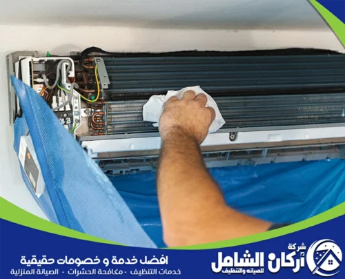 تنظيف الوحدة الداخلية لمكيف سبليت من الداخل باستخدام قطعة قماش، مع حماية الجدار بغطاء أزرق أثناء إزالة الأتربة من المبادل الحراري وأجزاء المكيف الداخلية.